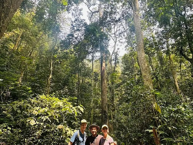 Drei lächelnde Touristen posieren in einem dichten, hohen Tropenwald in Cuc Phuong