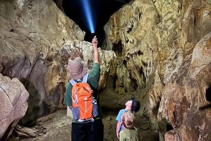 Homme utilisant une lampe torche pour montrer des stalactites à des enfants dans une grande grotte
